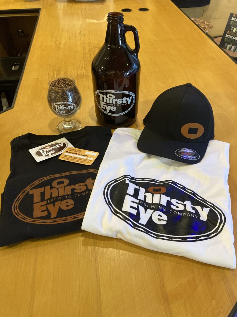 photo of merchandise including t-shirts, growler, goblet glass and stickers.