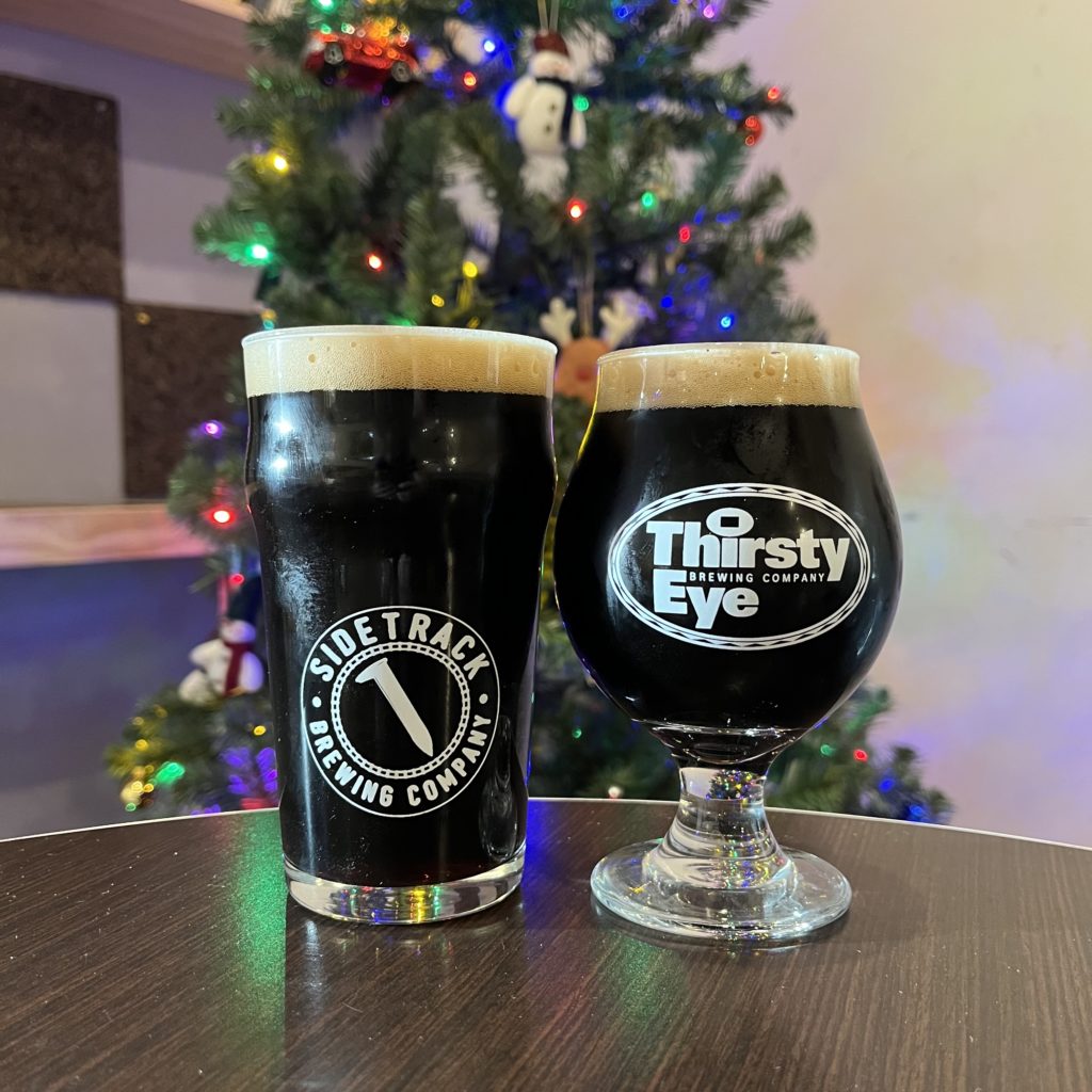 Two glasses of dark peppermint porter on a table in front of a christmas tree
